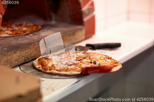 Image of baked pizza on peel and oven at pizzeria