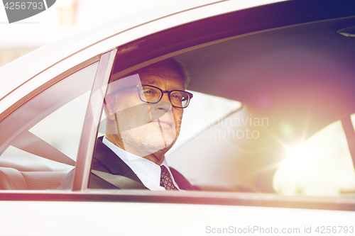 Image of senior businessman driving on car back seat