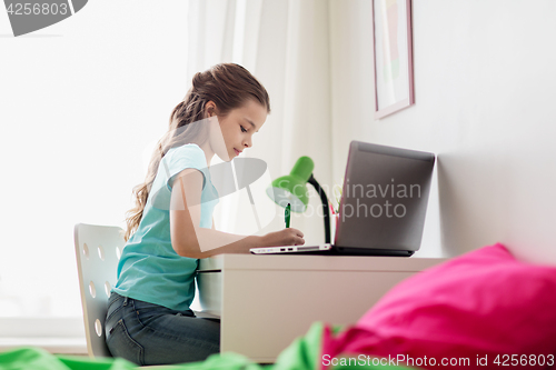 Image of girl with laptop writing to notebook at home