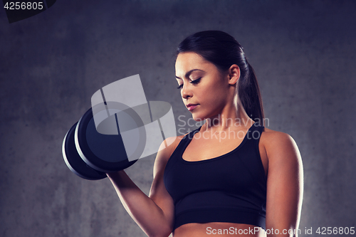 Image of young woman flexing muscles with dumbbells in gym