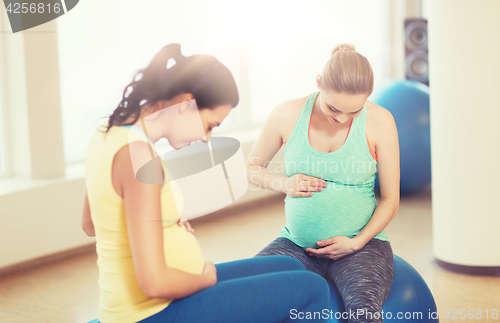 Image of two happy pregnant women sitting on balls in gym