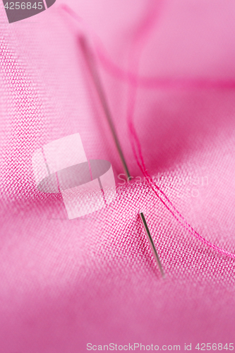 Image of sewing needle with thread stuck into pink fabric