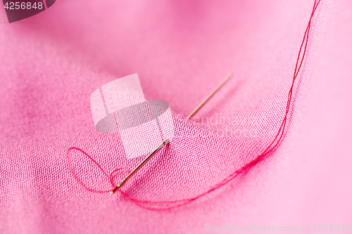 Image of sewing needle with thread stuck into pink fabric