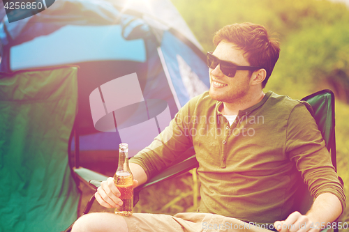 Image of happy young man drinking beer at campsite tent