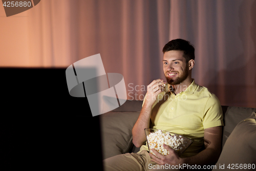 Image of happy man with popcorn watching tv at night
