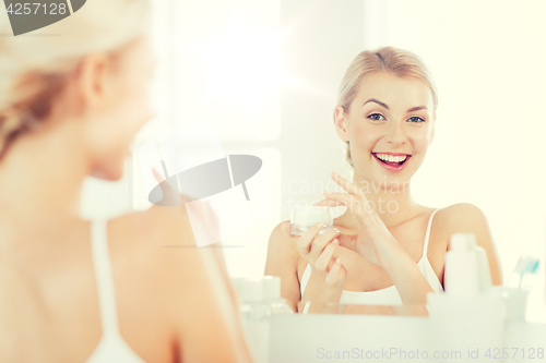 Image of happy woman applying cream to face at bathroom