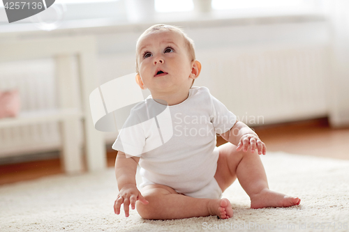 Image of happy baby boy or girl sitting on floor at home
