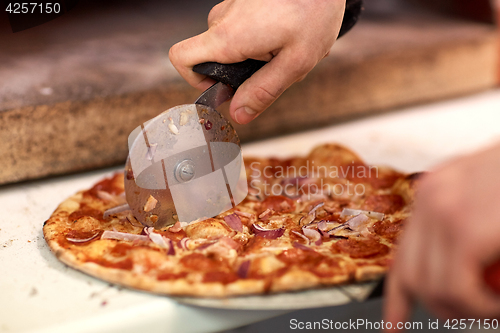 Image of cook hands cutting pizza to pieces at pizzeria