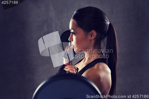 Image of young woman flexing muscles with barbell in gym