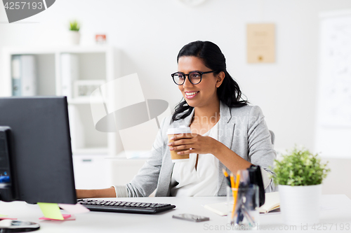 Image of businesswoman drinking coffee at office computer