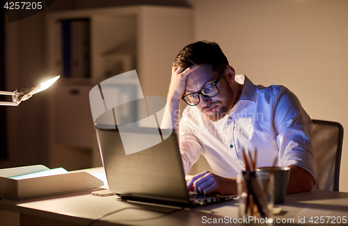 Image of businessman with laptop thinking at night office