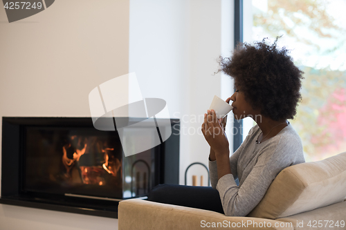 Image of black woman drinking coffee in front of fireplace