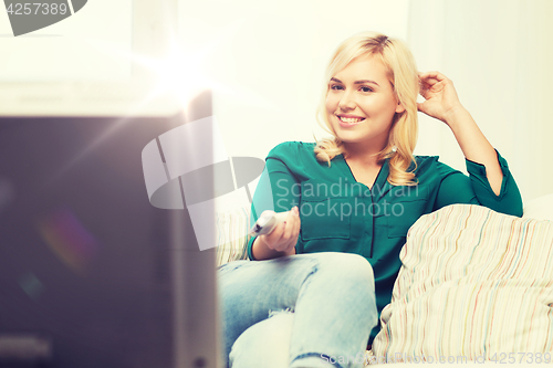 Image of smiling woman with remote watching tv at home