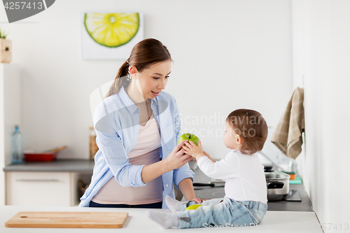 Image of mother giving green apple to baby at home kitchen