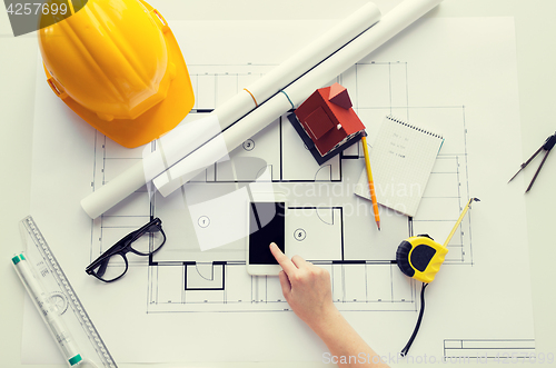 Image of close up of hand with blueprint and smartphone