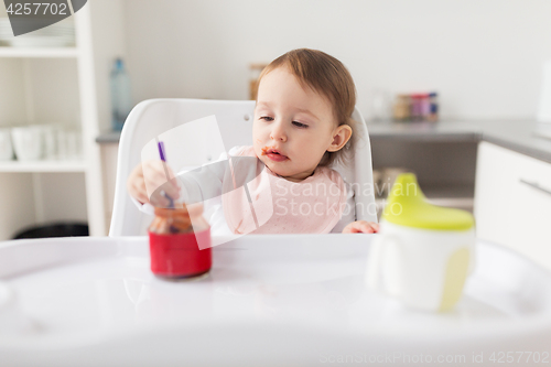 Image of baby girl with spoon eating puree from jar at home
