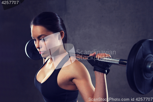 Image of young woman flexing muscles with barbell in gym