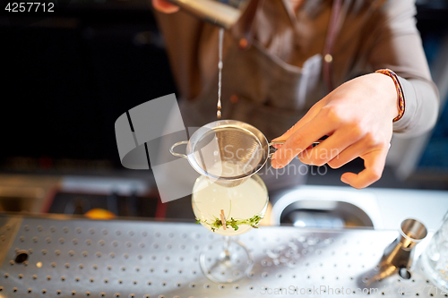 Image of woman bartender pouring cocktail into glass at bar