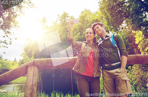 Image of couple with backpacks taking selfie by smartphone