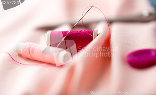 Image of sewing needle, spools of thread and cloth