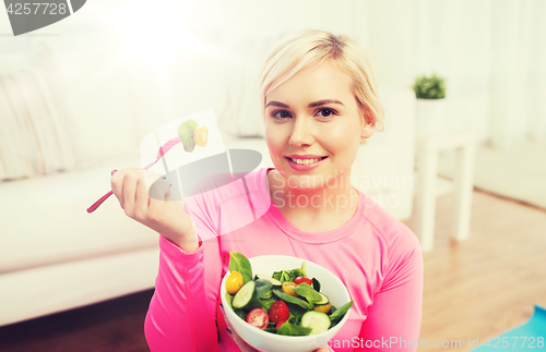 Image of smiling young woman eating salad at home
