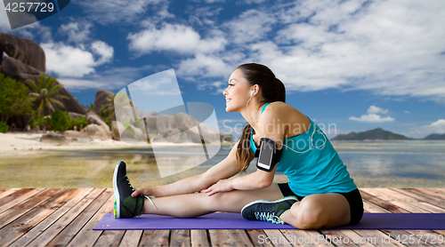 Image of woman with smartphone stretching leg on mat