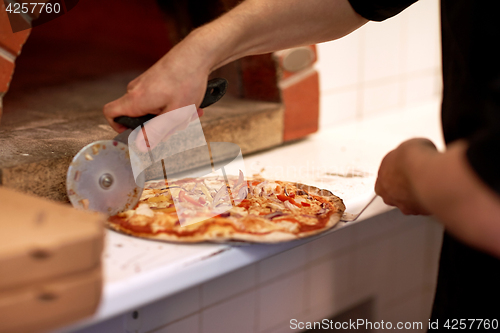 Image of cook hands cutting pizza to pieces at pizzeria