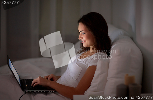 Image of happy woman with laptop in bed at home bedroom