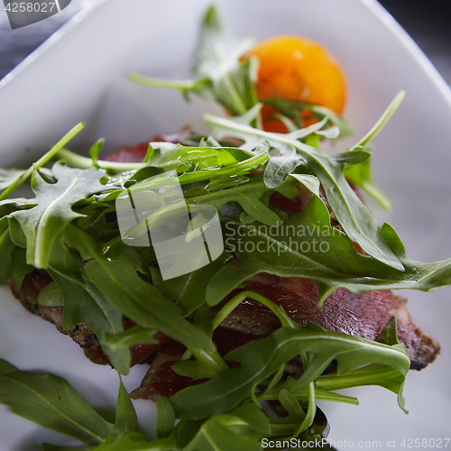 Image of slice of prosciutto or jamon with arugula leafs