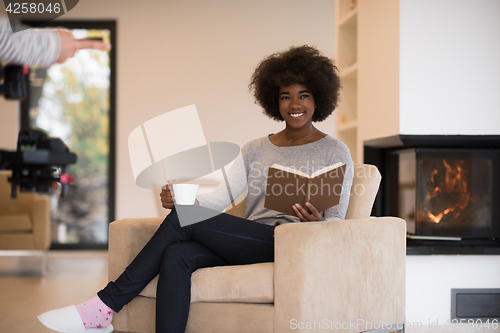 Image of black woman reading book  in front of fireplace