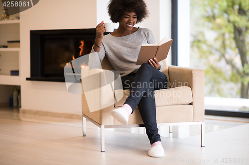 Image of black woman reading book  in front of fireplace