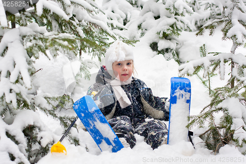 Image of little girl in skiing sits on the snow