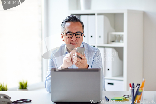 Image of businessman with laptop texting on smartphone