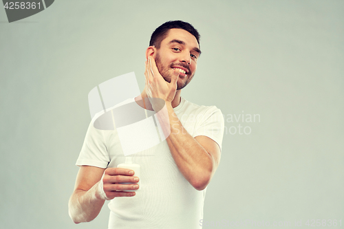 Image of happy young man applying cream or lotion to face