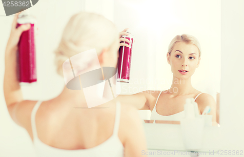 Image of woman with hairspray styling her hair at bathroom