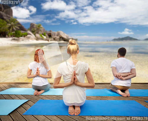 Image of group of people making yoga exercises over beach