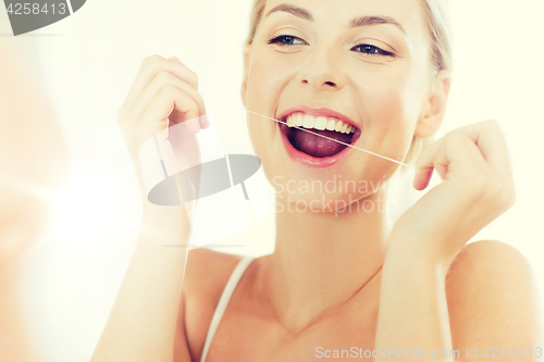 Image of woman with dental floss cleaning teeth at bathroom