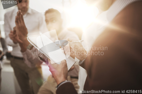 Image of business team and man writing to notepad at office