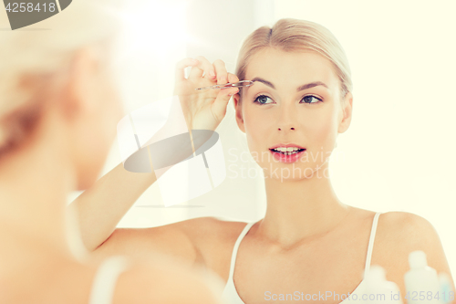 Image of woman with tweezers tweezing eyebrow at bathroom