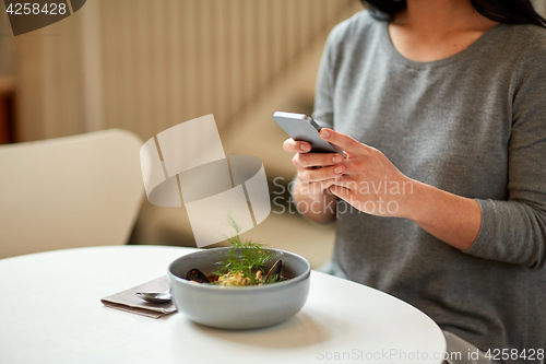 Image of woman with smartphone and bowl of soup at cafe