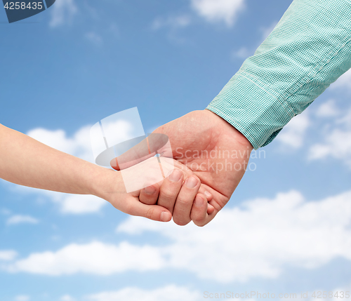 Image of father and child holding hands over blue sky