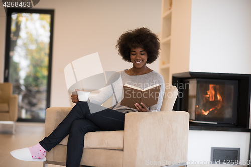 Image of black woman reading book  in front of fireplace