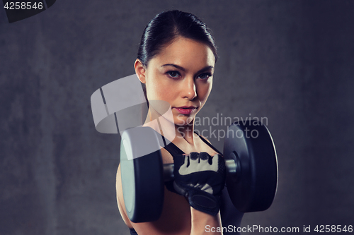 Image of young woman flexing muscles with dumbbells in gym