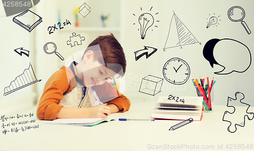 Image of smiling student boy writing to notebook at home