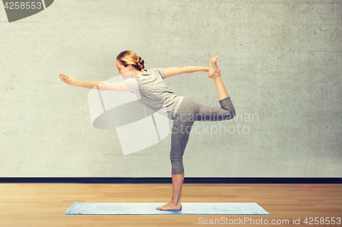 Image of woman making yoga in lord of the dance pose on mat