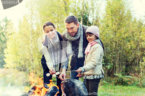 Image of happy family roasting marshmallow over campfire