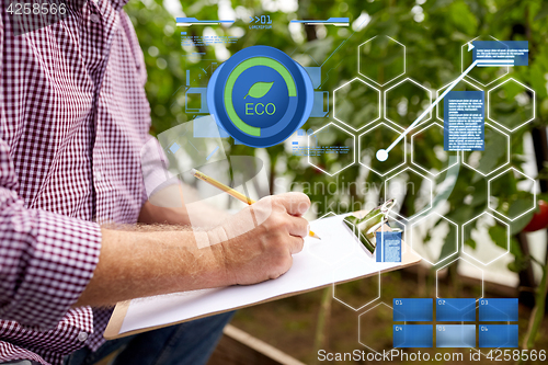 Image of senior man writing to clipboard at farm greenhouse