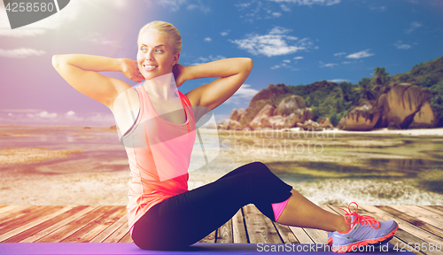 Image of smiling woman exercising on mat outdoors
