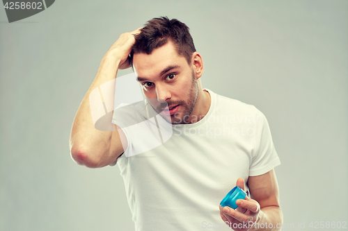 Image of happy young man styling his hair with wax or gel