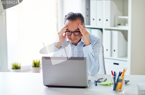 Image of businessman in eyeglasses with laptop at office